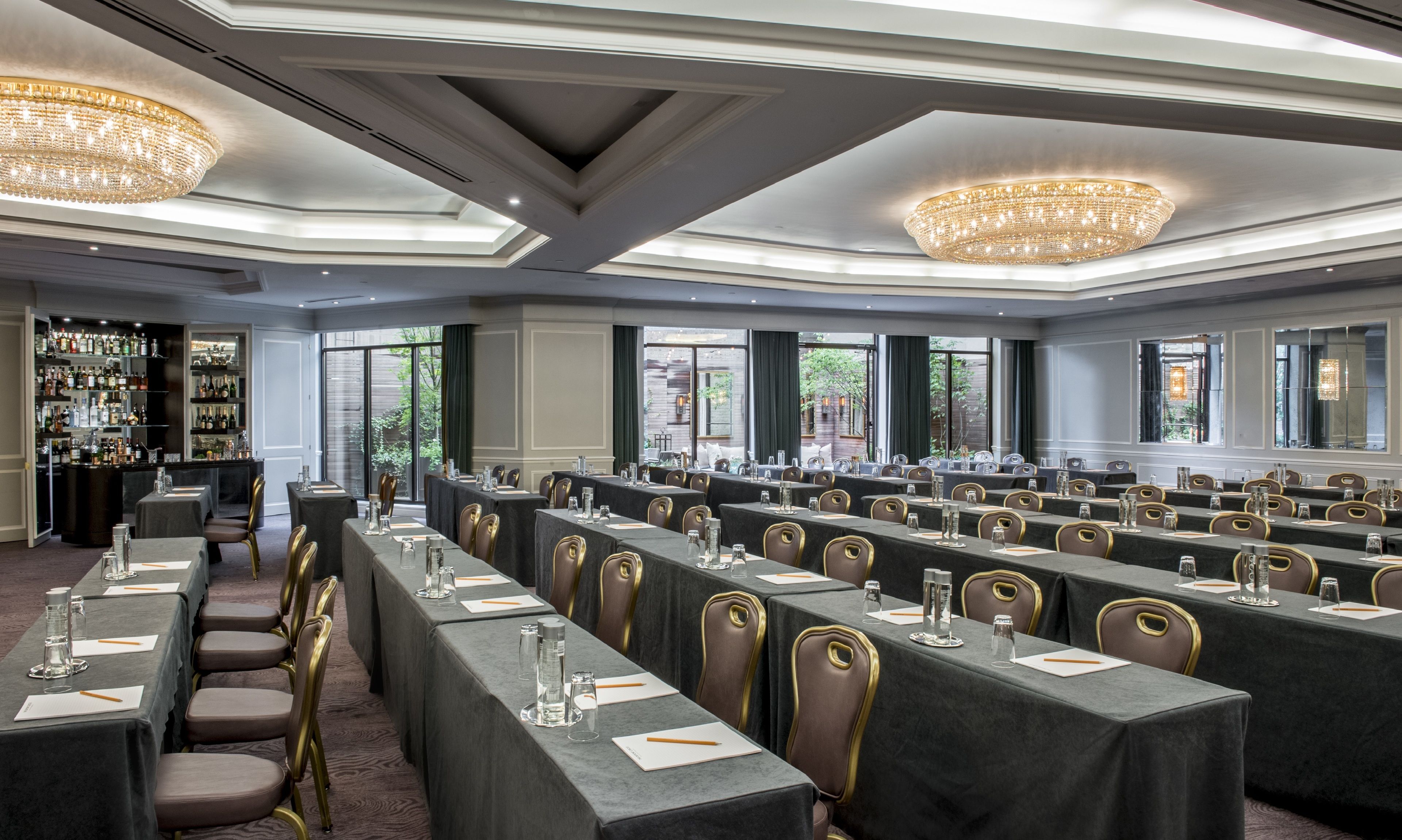 Sala de conferências com mesas compridas, cadeiras e um espaço bar com prateleiras de garrafas.