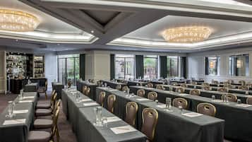 Sala de conferências com mesas compridas, cadeiras e um espaço bar com prateleiras de garrafas.