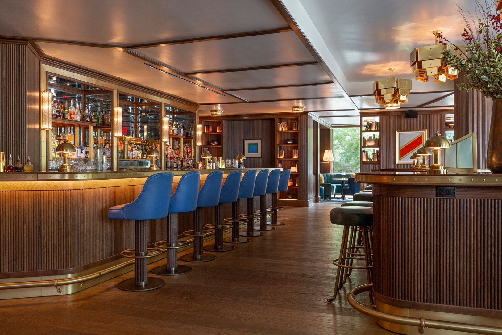 A bar area with a long counter, blue bar stools, and a variety of bottles and glasses.