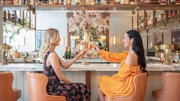 Two women seated at a bar with a variety of liquor bottles on shelves behind them.
