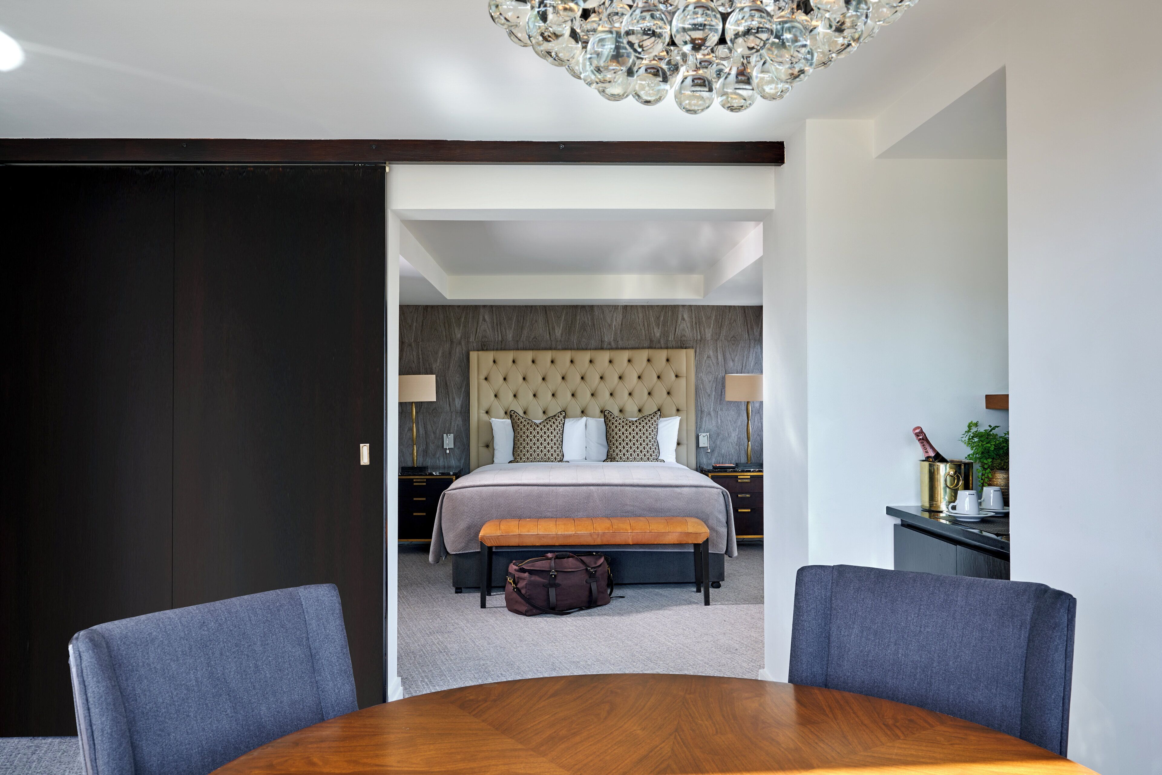 A modern hotel room with a large bed, a wooden dining table, and a bench.