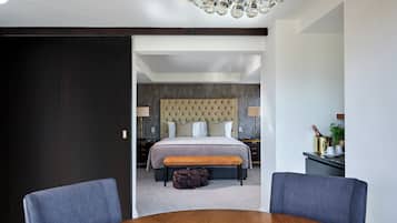 A modern hotel room with a large bed, a wooden dining table, and a bench.