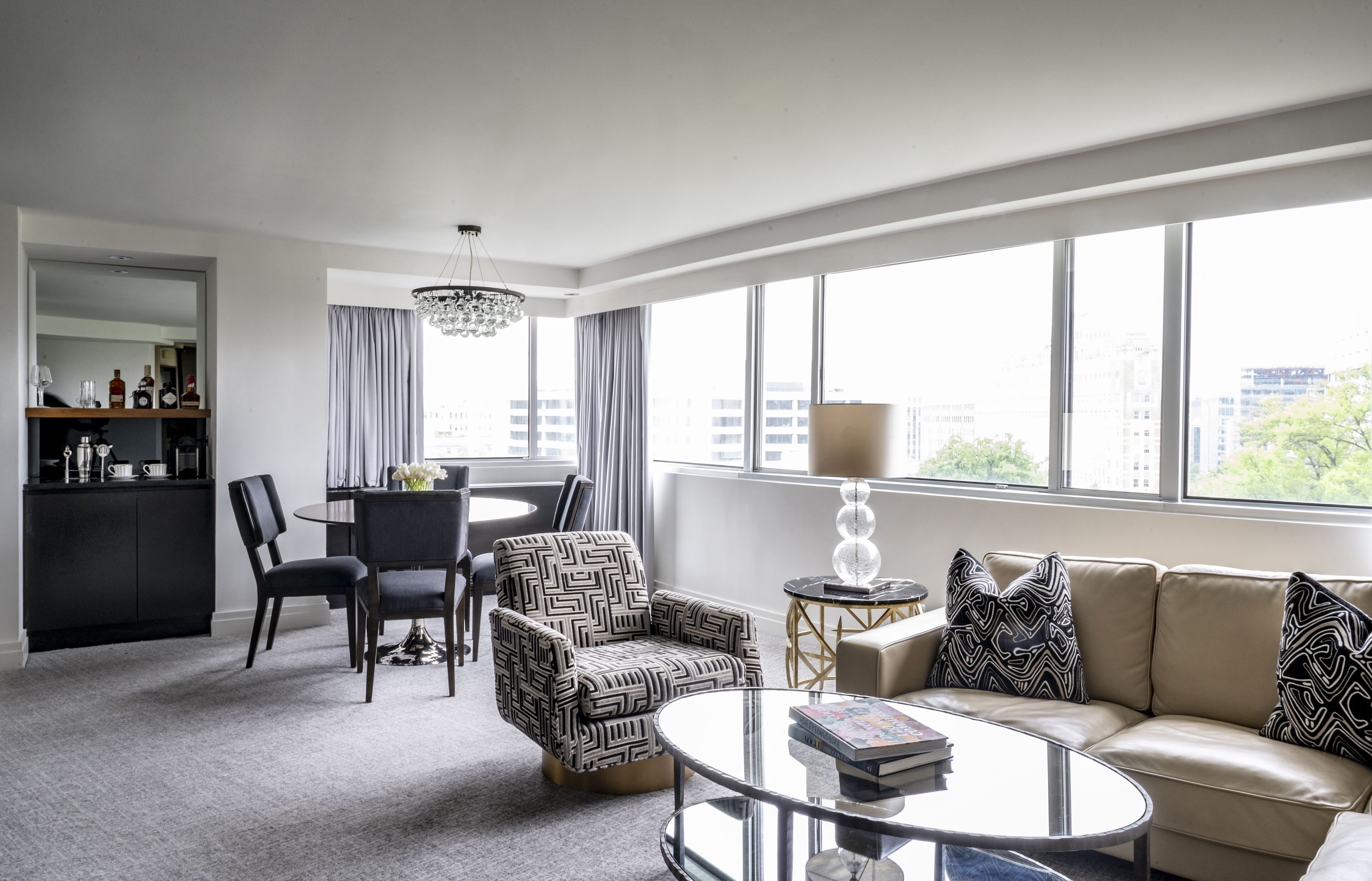 Une chambre d’hôtel moderne dotée d’un coin repas, d’un canapé et d’une grande fenêtre offrant une vue sur la ville.