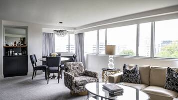 Une chambre d’hôtel moderne dotée d’un coin repas, d’un canapé et d’une grande fenêtre offrant une vue sur la ville.