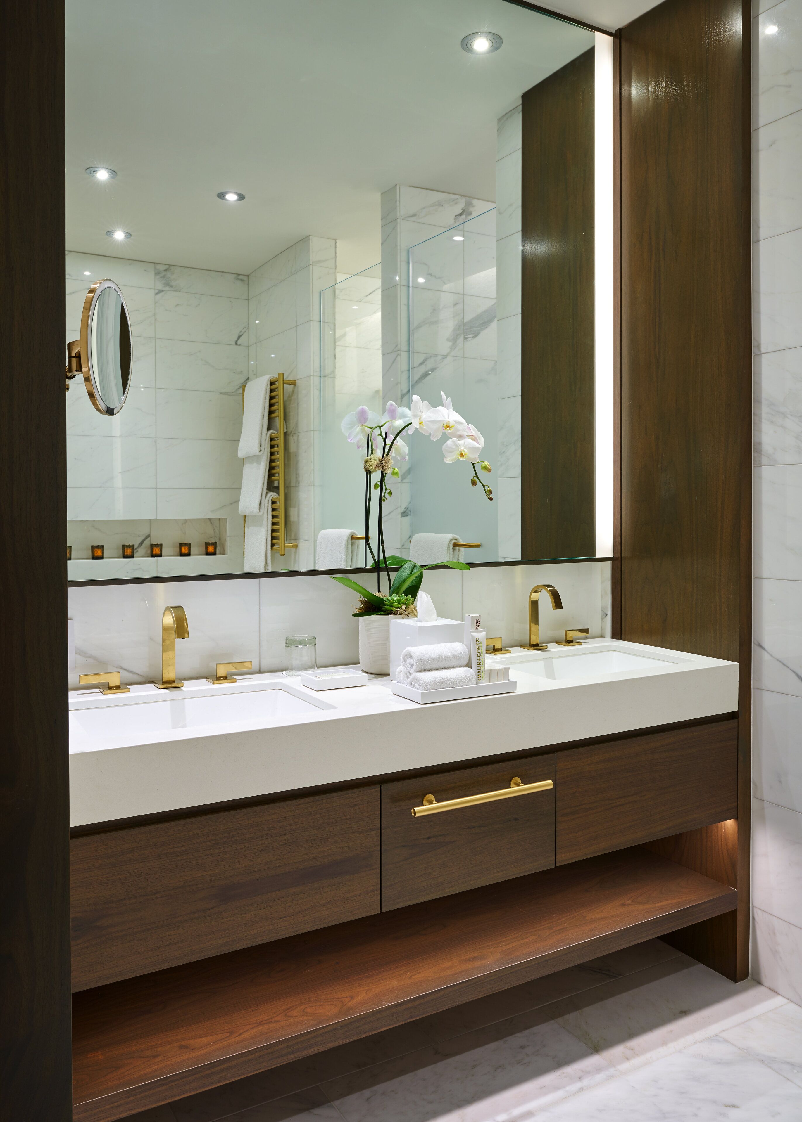Un bagno moderno con doppio lavabo, accessori dorati, un ampio specchio e un'orchidea in vaso.