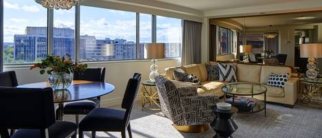 A modern hotel room with a large window, a dining area, a sofa set, and a small coffee table.