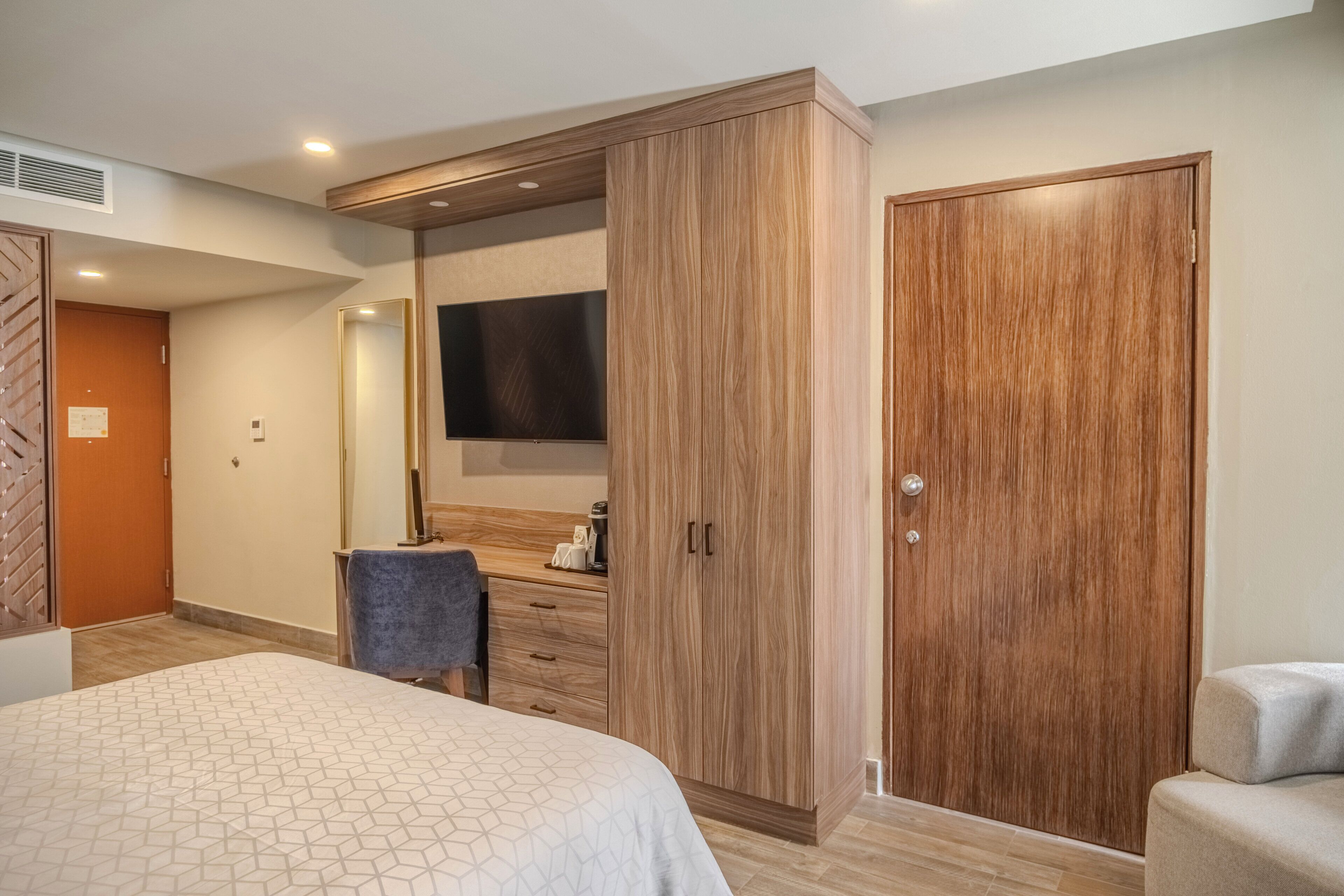 Un dormitorio con cama, armario, escritorio con silla y televisor montado en la pared.