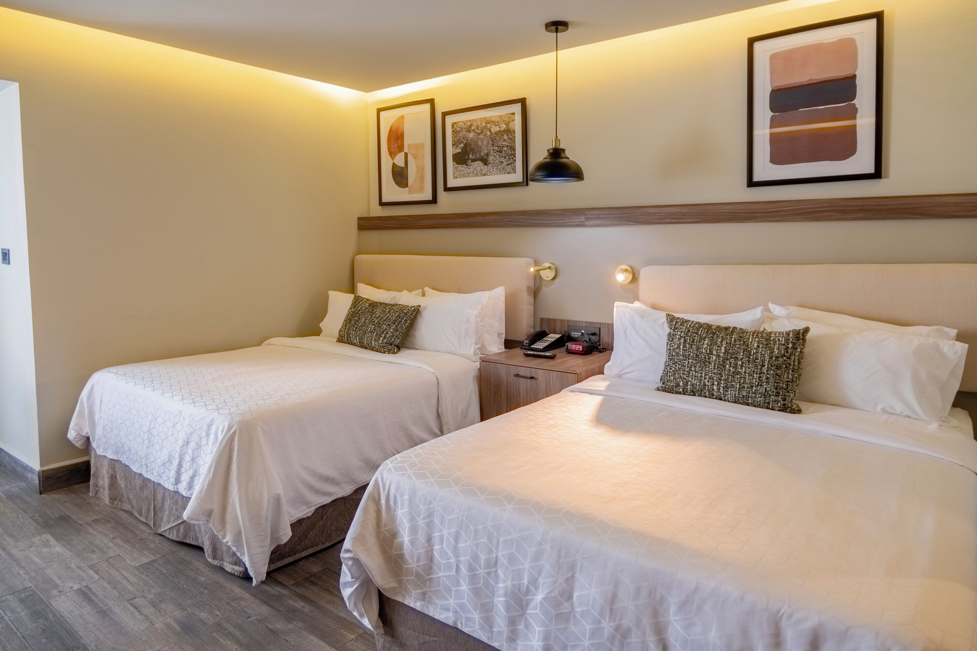 Habitación de hotel con dos camas, una mesita de noche con teléfono y obras de arte colgadas en la pared.