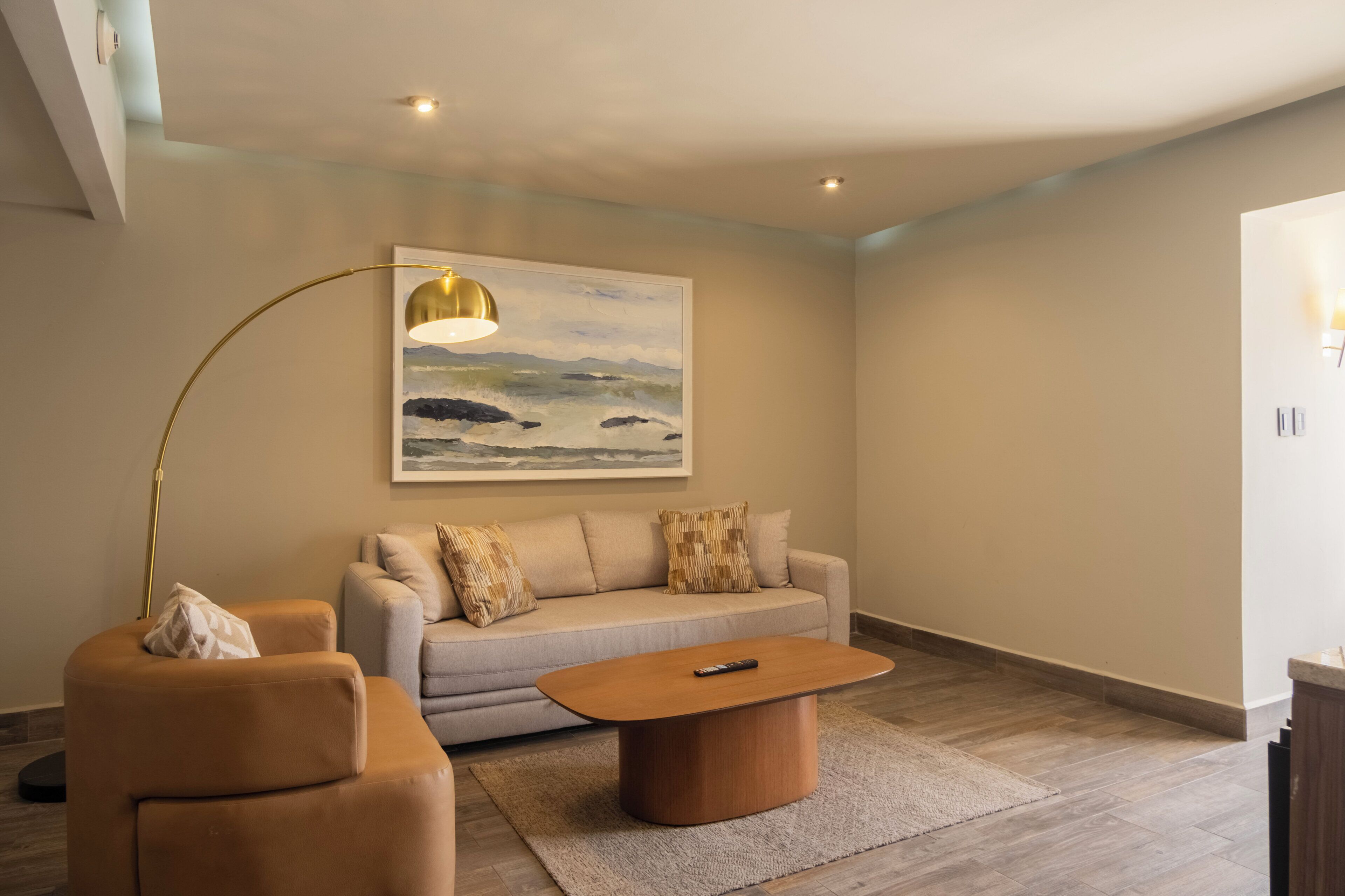 A modern living room with a sofa, armchair, coffee table, and a painting of a landscape.