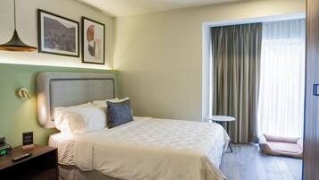 Habitación de hotel con cama, mesita de noche, lámpara, cuadros enmarcados y vistas al exterior.