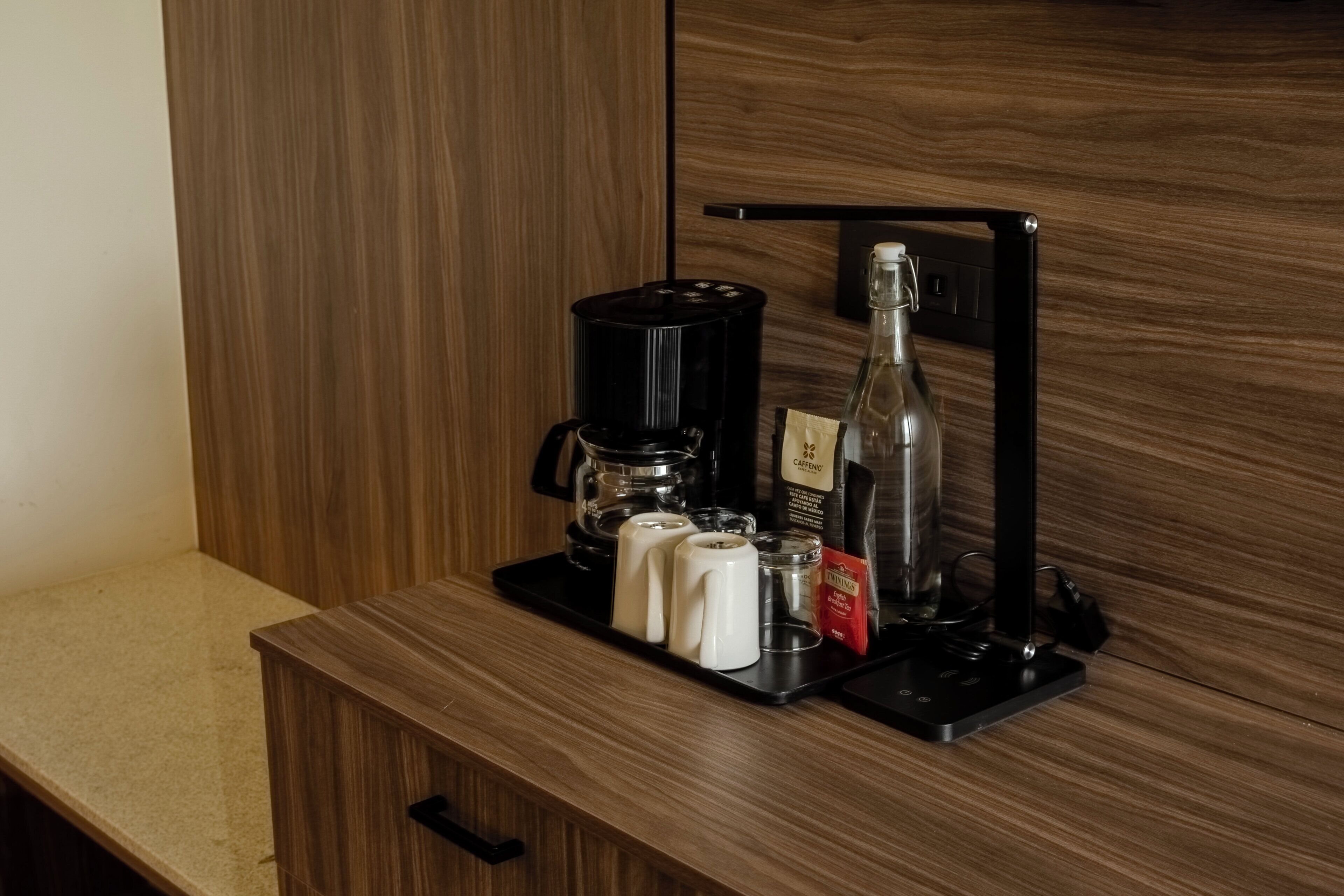A coffee station with a coffee maker, a bottle, and a cup on a tray.