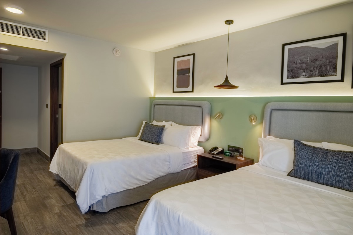A hotel room with two beds, a desk, a chair, a phone, and a picture on the wall.