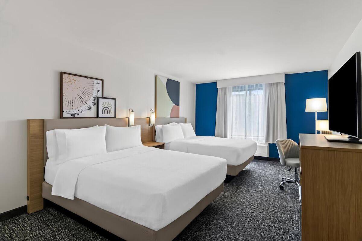 Een hotelkamer met twee bedden, een bureau, een stoel en kunstwerken aan de wanden.