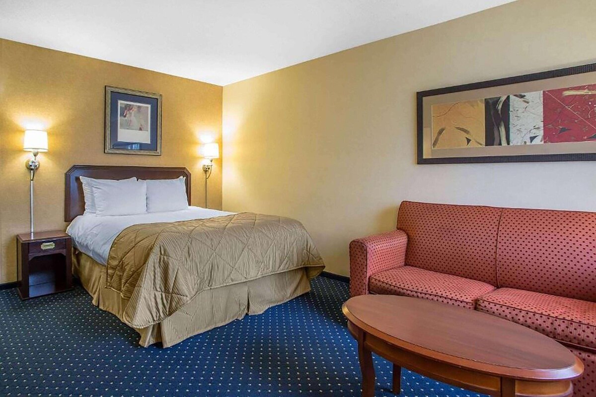 A hotel room with a bed, a sofa, a small table, two bedside lamps, and artwork on the walls.