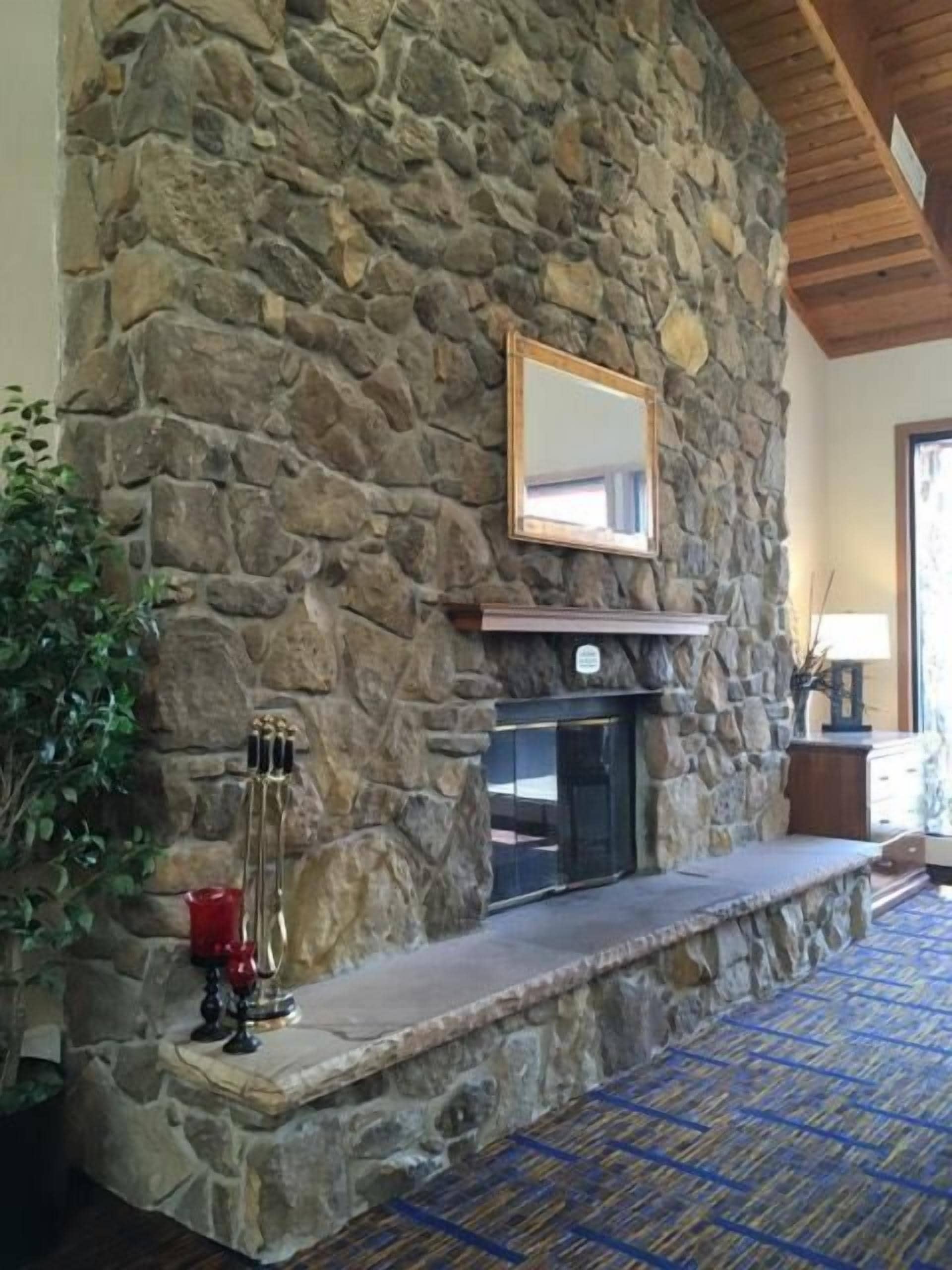 A stone fireplace with a mantel, a mirror, and a red candle holder.