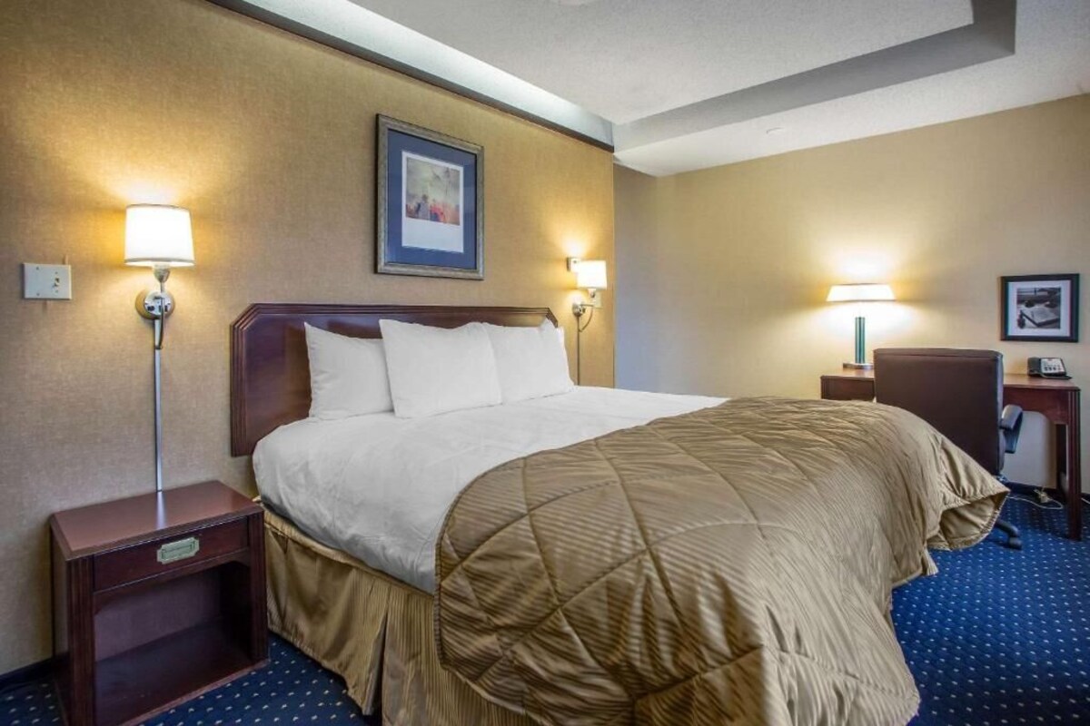 A hotel room with a large bed, two bedside lamps, a nightstand, a desk, and a framed picture on the wall.