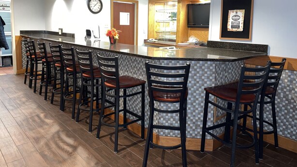A modern kitchen with a bar area, wooden ceiling beams, and a tiled backsplash. - Clarion Inn (Merrillville)
