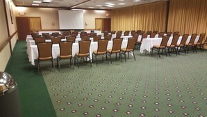 A conference room with rows of tables and chairs, a projector screen, and a green carpeted floor. - Clarion Inn (Merrillville)