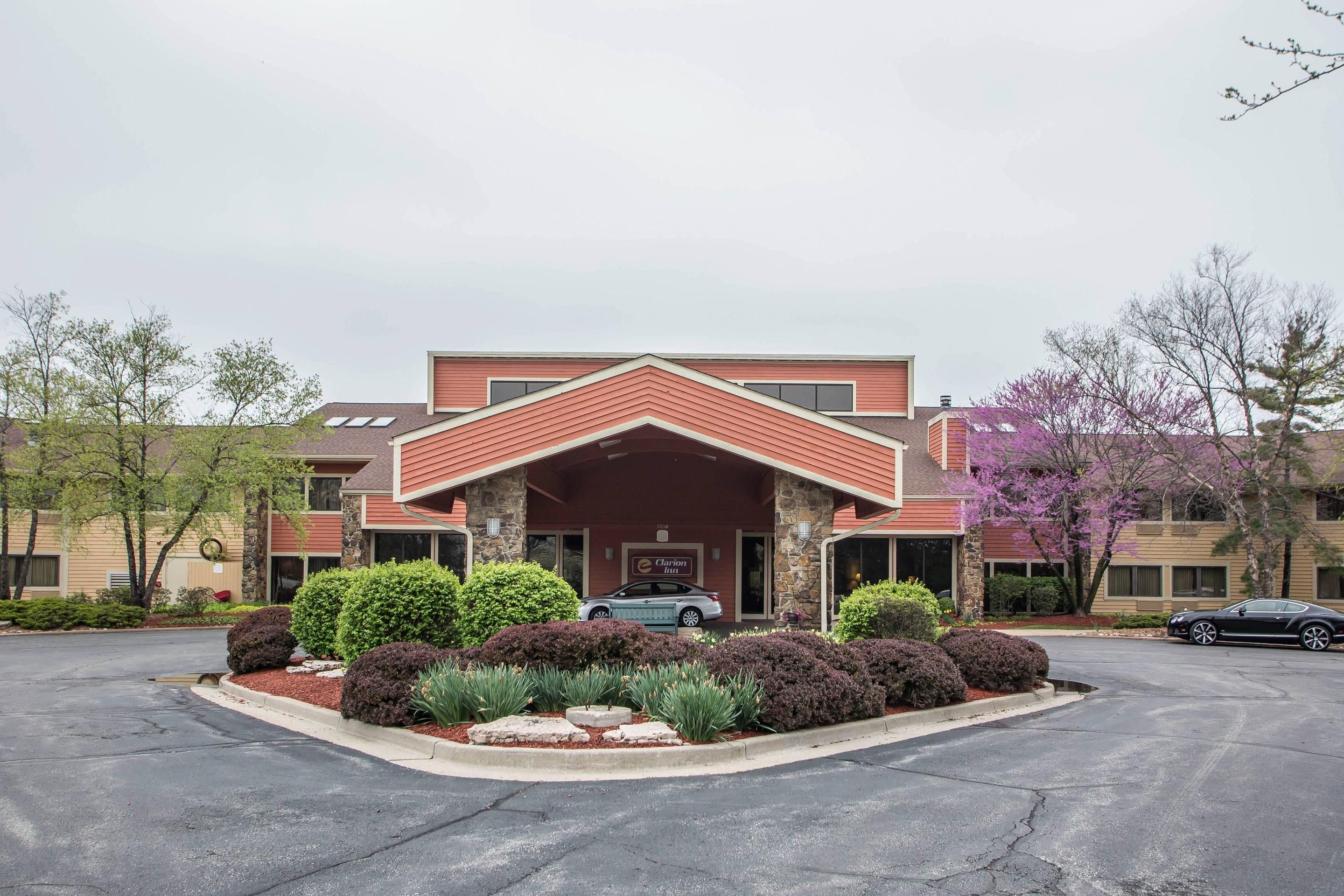 A hotel with a red roof and stone facade, a parking lot, and surrounding greenery.