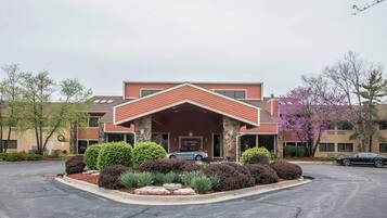 A hotel with a red roof and stone facade, a parking lot, and surrounding greenery.