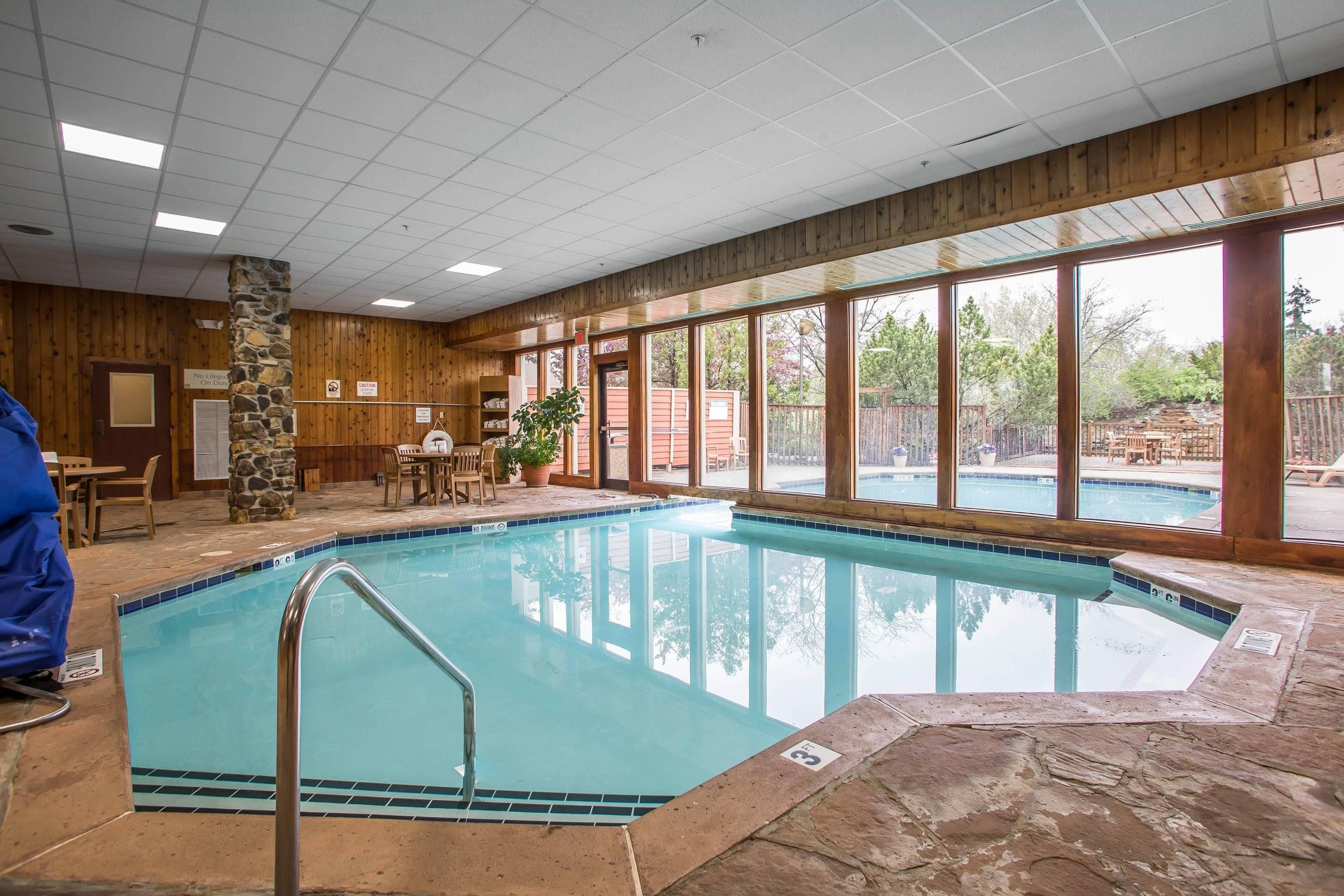 Ein Hallenbad mit Steinwand, Holzbalkendecke und großen Fenstern.