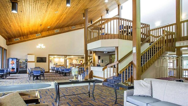 A spacious lobby with a high wooden ceiling, a staircase, and a seating area with a sofa and coffee table. - Howard Johnson by Wyndham Merrillville (Merrillville)