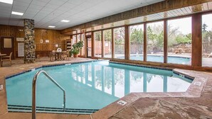 An indoor swimming pool with a stone border, wooden walls, and large windows offering a view of the outdoors. - Howard Johnson by Wyndham Merrillville (Merrillville)