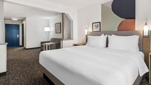 A hotel room with a large bed, a desk, a chair, and a painting on the wall. - Howard Johnson by Wyndham Merrillville (Merrillville)