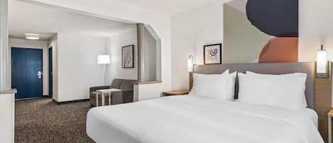 A hotel room with a large bed, a desk, a chair, and a painting on the wall.