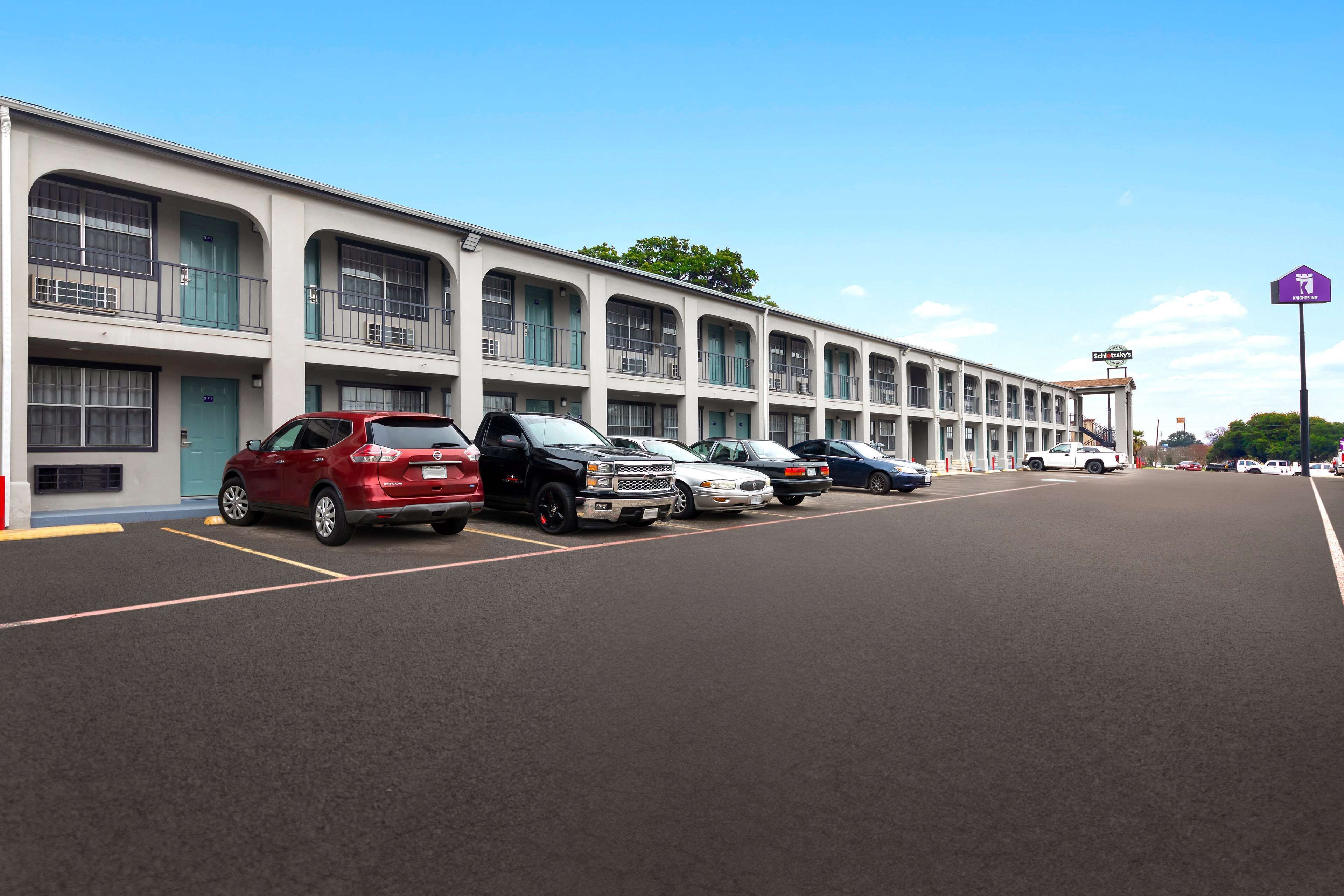 A row of parked cars in front of a motel with multiple balconies and a clear sky.