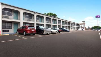 A row of parked cars in front of a motel with multiple balconies and a clear sky.