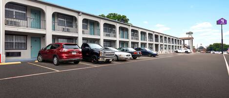 A row of parked cars in front of a motel with multiple balconies and a clear sky.