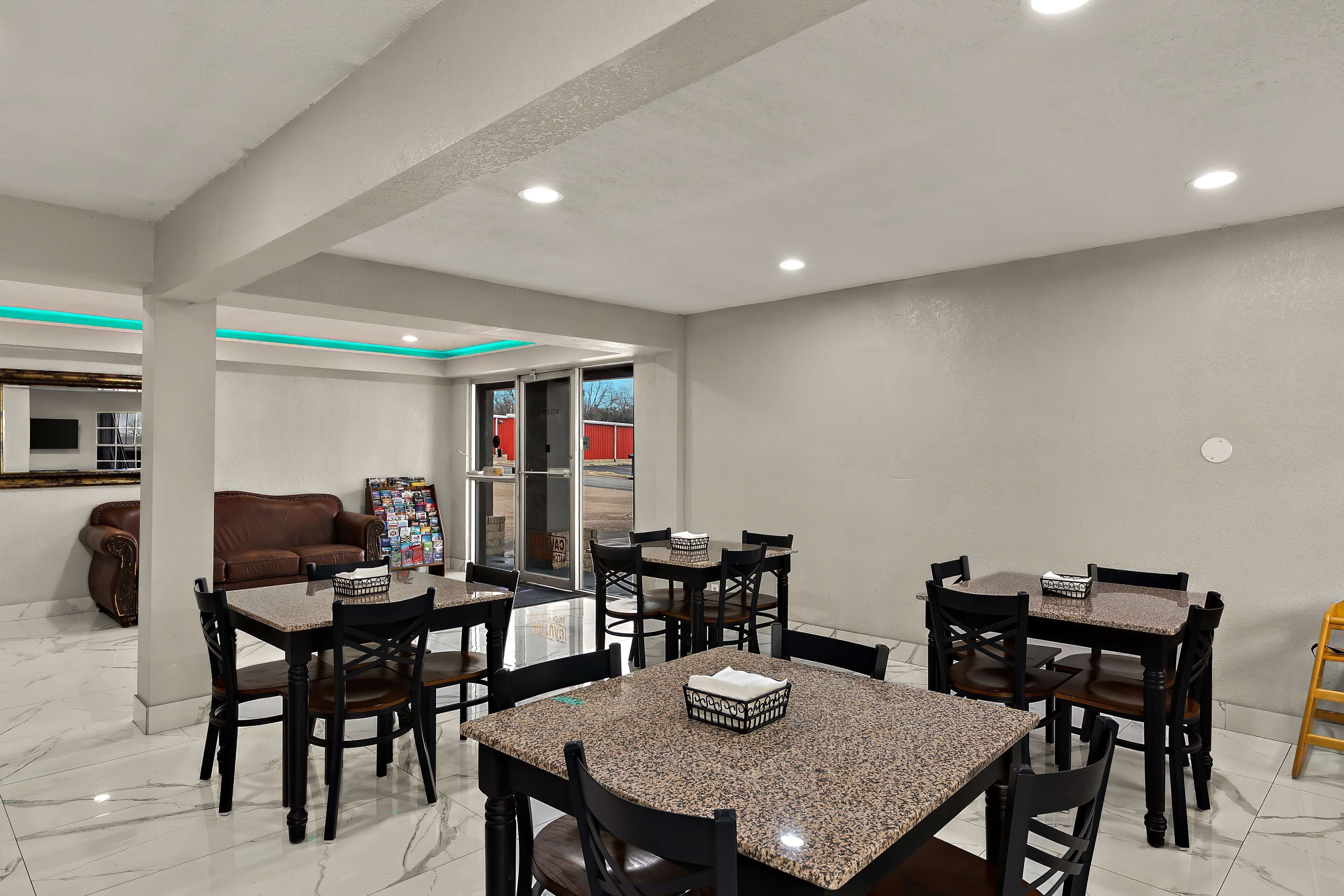 A dining area with marble flooring, wooden tables and chairs, and a brown leather sofa.