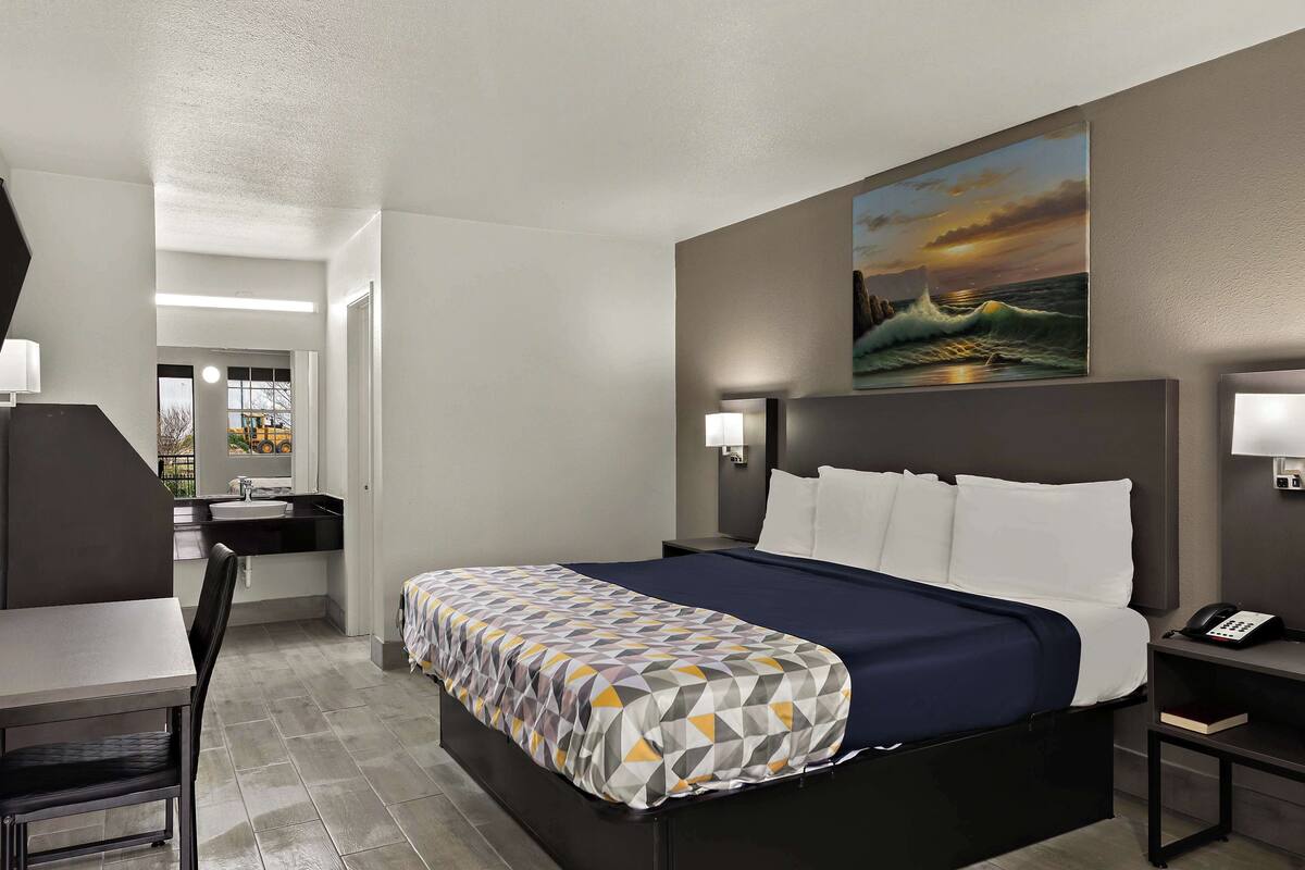 Una habitación de hotel con cama, mesita de noche, lámpara y un cuadro en la pared.