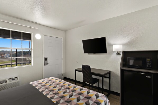 A hotel room with a bed, a desk, a chair, a TV, a microwave, and a window with a view of the outside. - Knights Inn Belton (Belton)