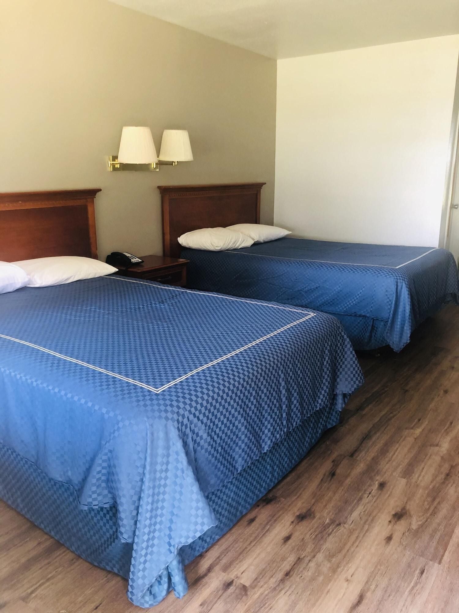 Ein Hotelzimmer mit zwei Betten, Holz-Kopfteilen, einem Nachttisch mit Telefon und Wandleuchten.