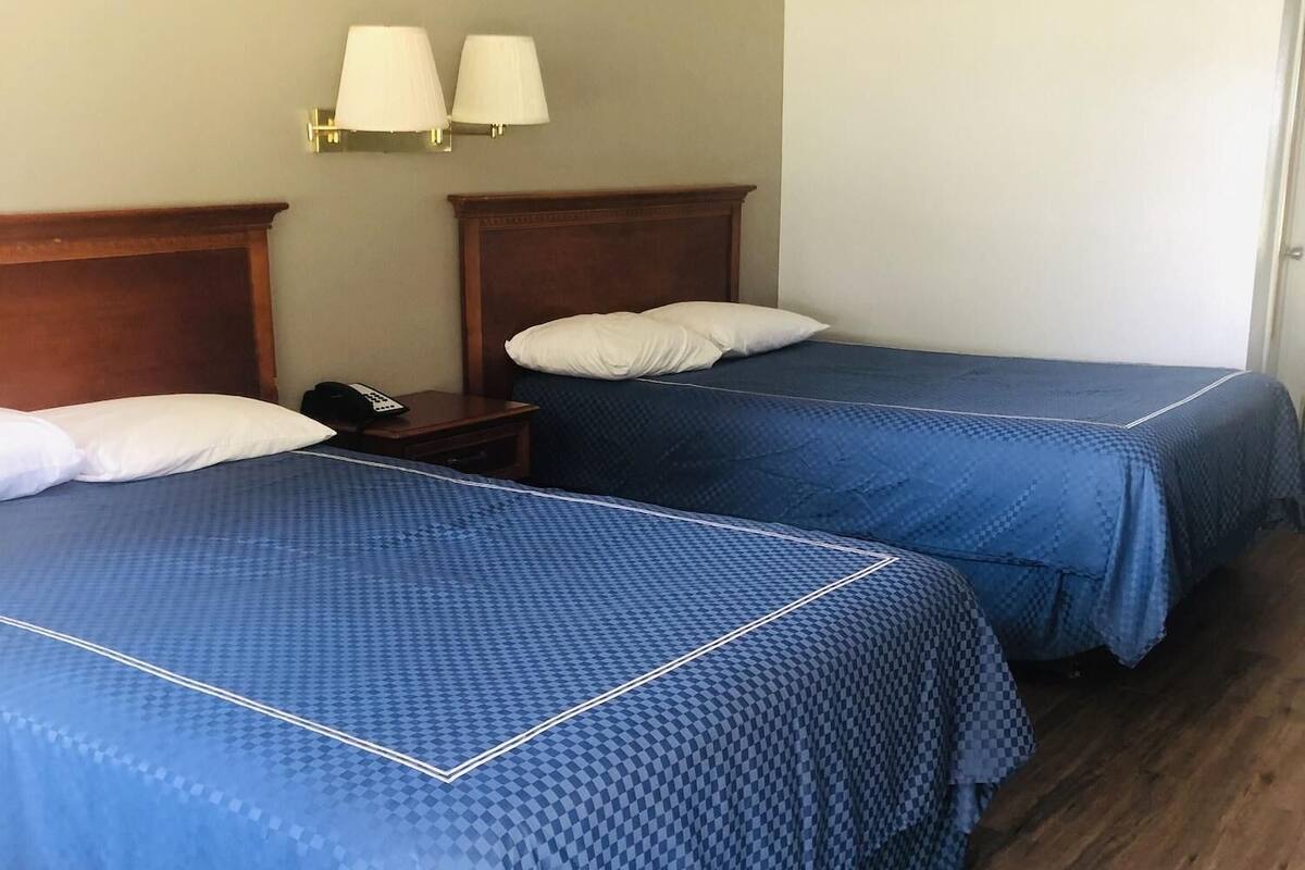 Habitación de hotel con dos camas, cabeceros de madera, una mesita de noche con teléfono y lámparas fijadas a la pared.
