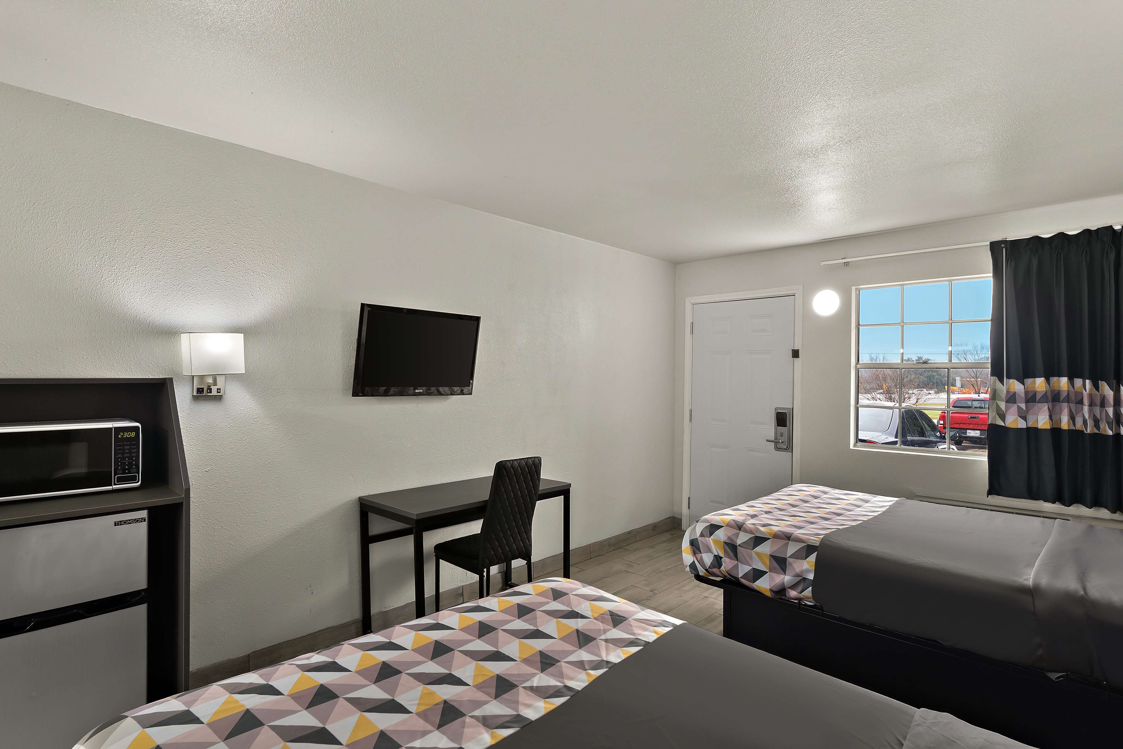 A hotel room with two beds, a desk, a chair, a microwave, a TV, and a window with curtains.