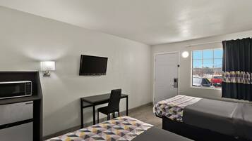 A hotel room with two beds, a desk, a chair, a microwave, a TV, and a window with curtains.