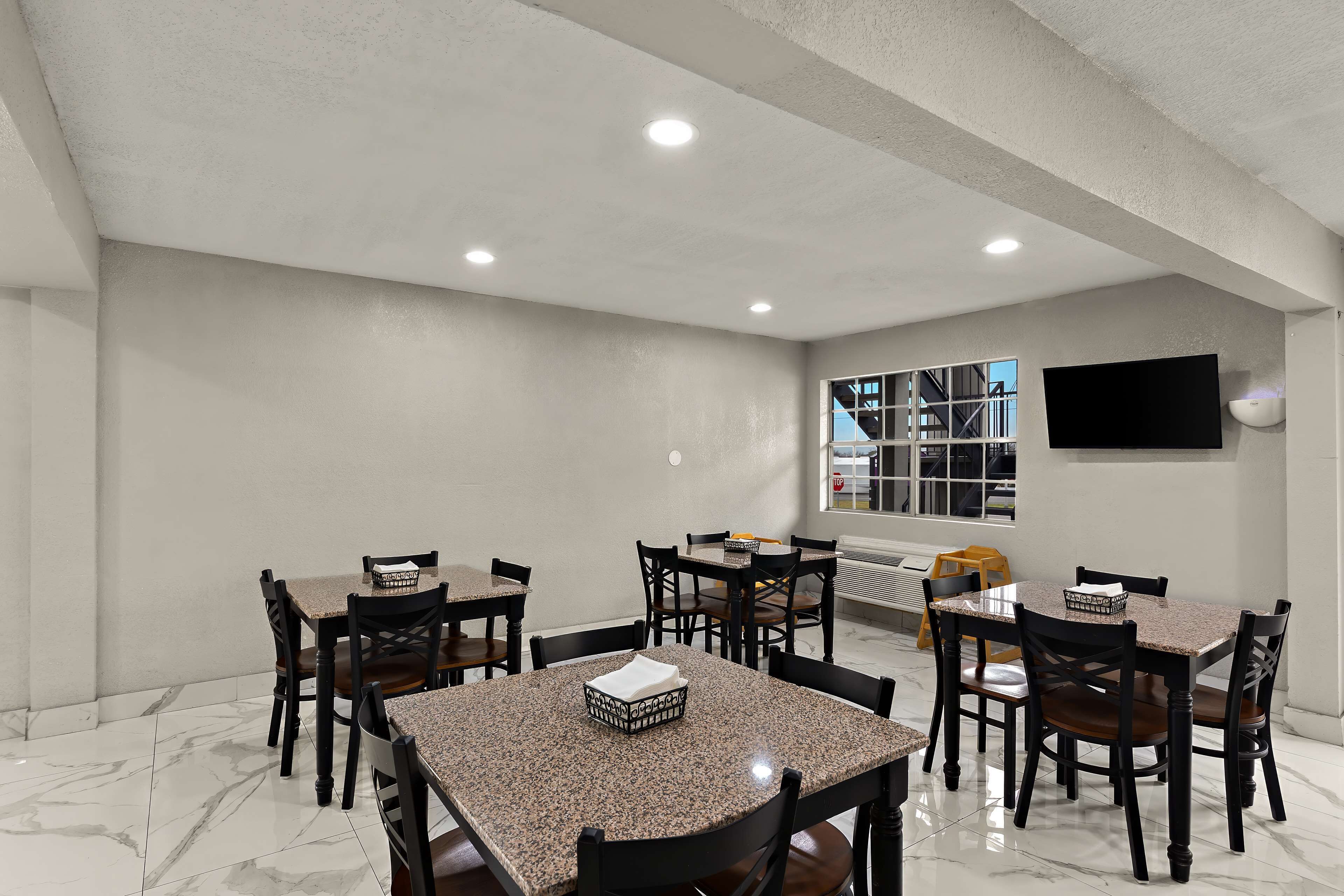 A dining area with multiple tables and chairs, a flat-screen TV mounted on the wall, and a window with a view of the outside.