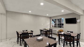 A dining area with multiple tables and chairs, a flat-screen TV mounted on the wall, and a window with a view of the outside.