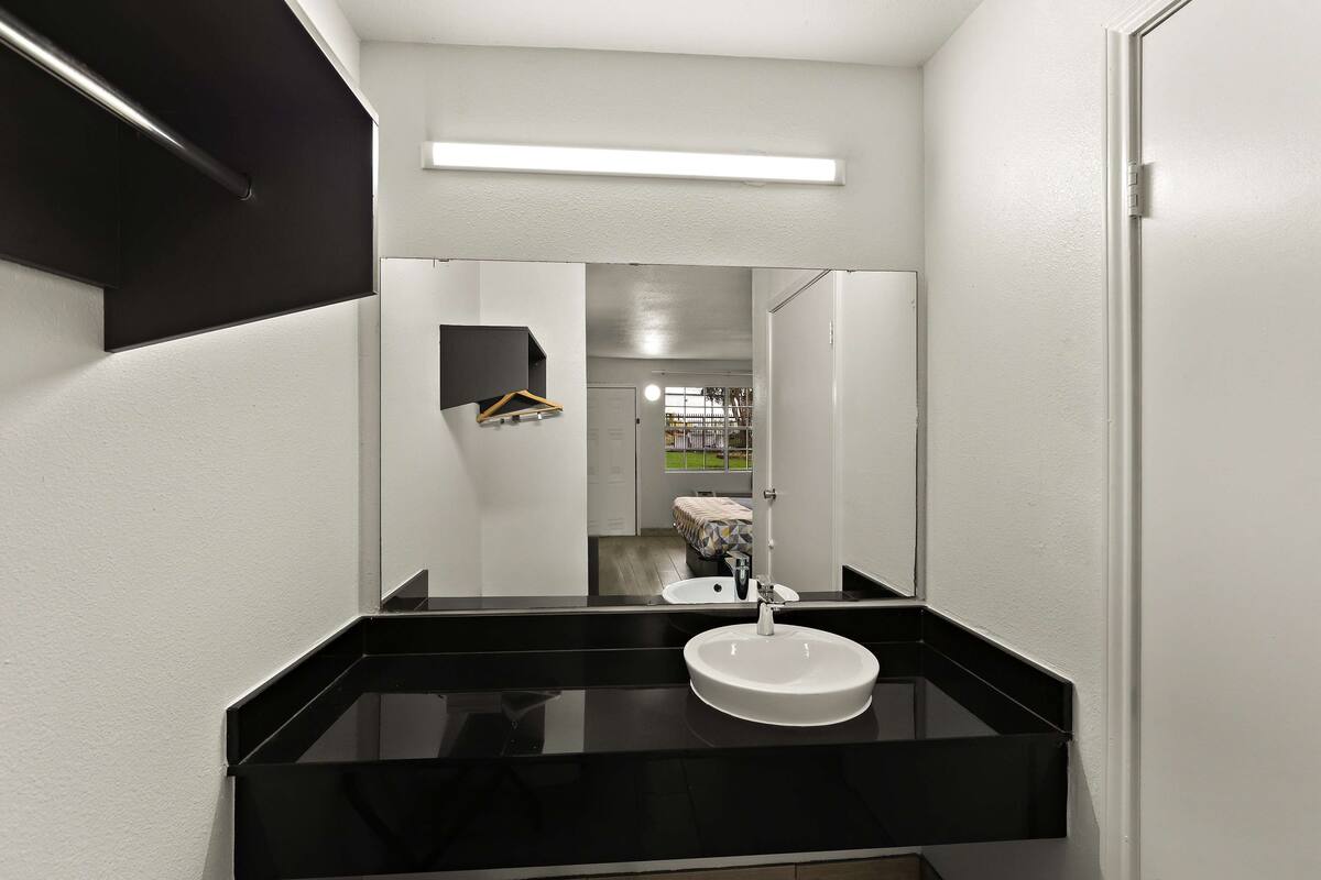 Un baño moderno con encimera negra, lavabo blanco y un espejo grande.