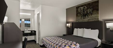 Une chambre d’hôtel moderne avec un grand lit, un bureau, une chaise, une salle de bain et un tableau représentant des éléphants au mur.