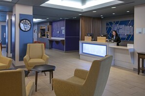 Een hotelhal met zitplaatsen, een receptiebalie en een klok aan de muur.