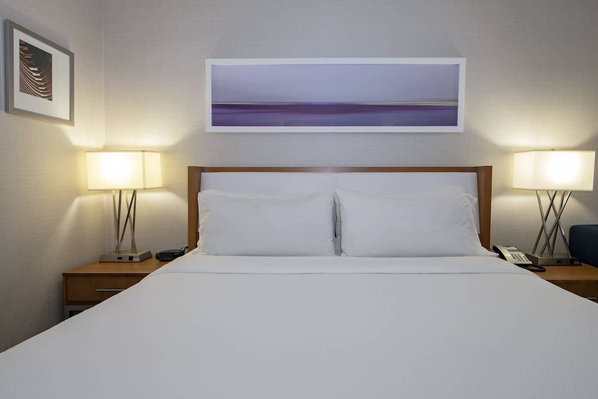 A hotel room with a large bed, two bedside tables with lamps, a painting above the bed, and a framed picture on the wall.