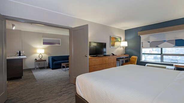 A hotel room with a bed, a desk with a TV, a sofa, a small table with a lamp, and a window with a view. - Holiday Inn Express Kamloops by IHG (Kamloops)