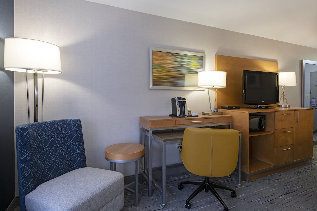 A hotel room with a desk, two chairs, a television, and a coffee machine.