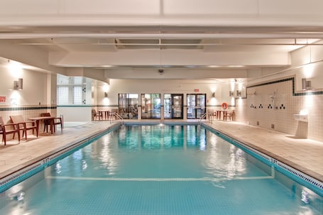 A swimming pool with clear blue water, surrounded by lounge chairs and tables.
