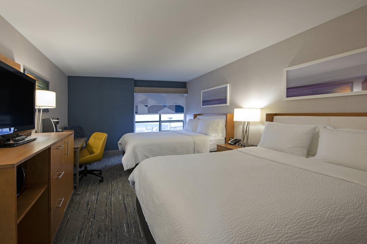 A hotel room with two beds, a desk with a computer, a chair, and a window with a view.