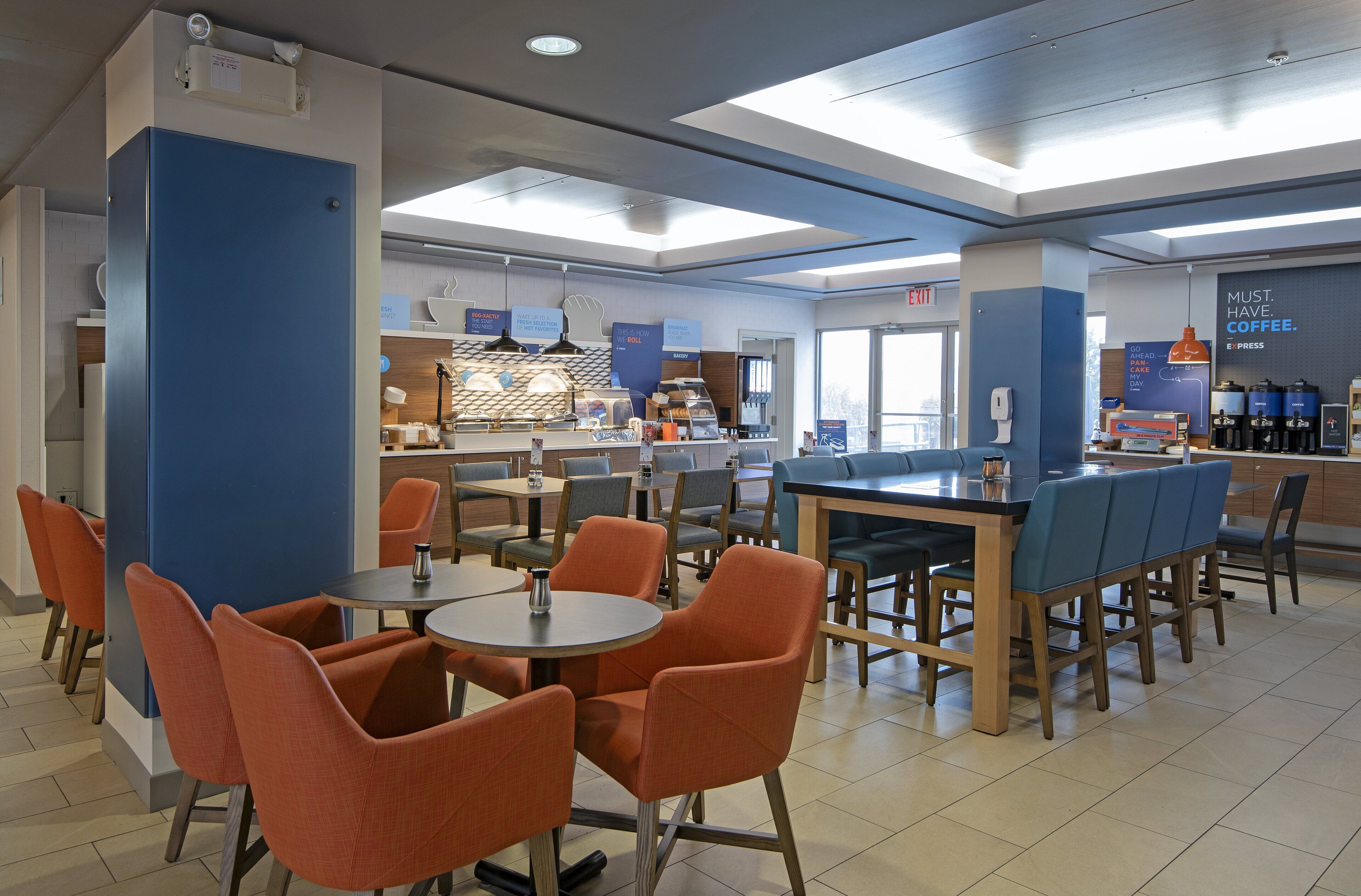 A modern cafe with round tables and orange chairs, a coffee bar, and a sign that says "MUST HAVE COFFEE."